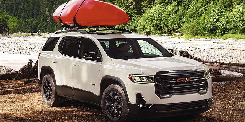 A red boat loaded on roof of white Acadia